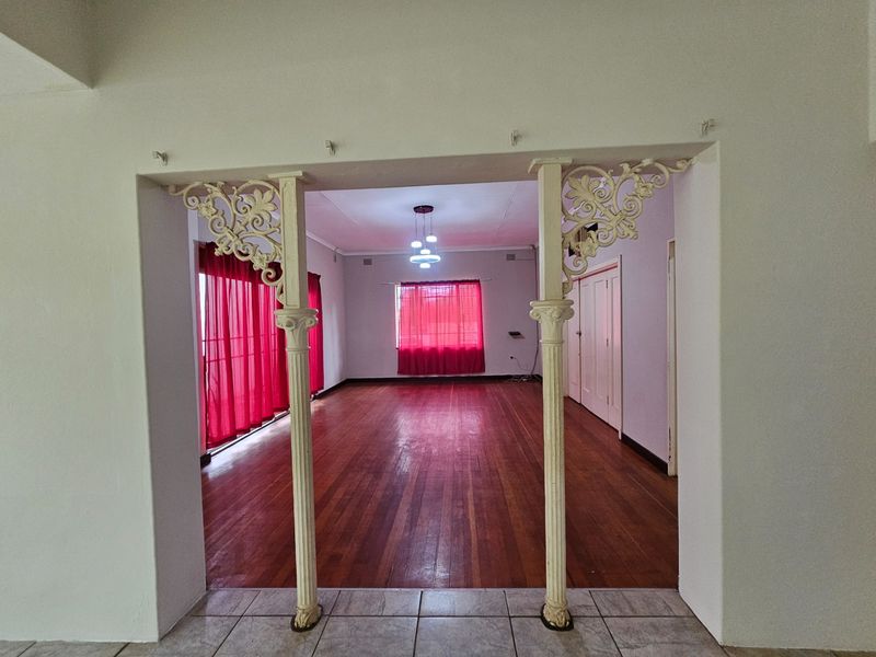 Spacious living area featuring original hardwood flooring and decorative cast iron columns, offering a blank canvas for interior design updates.