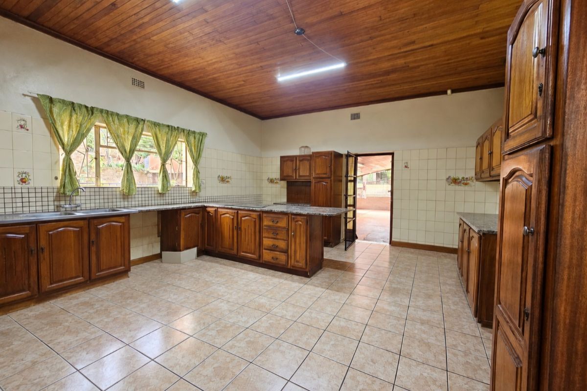 Spacious kitchen featuring traditional wooden cabinetry, granite countertops, tiled flooring, and a warm wooden ceiling, offering a functional layout with direct outdoor access.