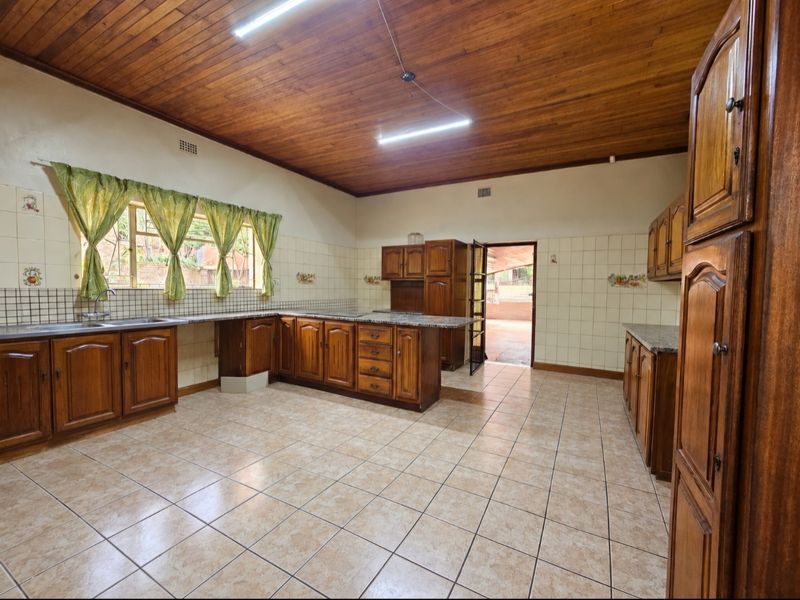 Spacious kitchen featuring traditional wooden cabinetry, granite countertops, tiled flooring, and a warm wooden ceiling, offering a functional layout with direct outdoor access.