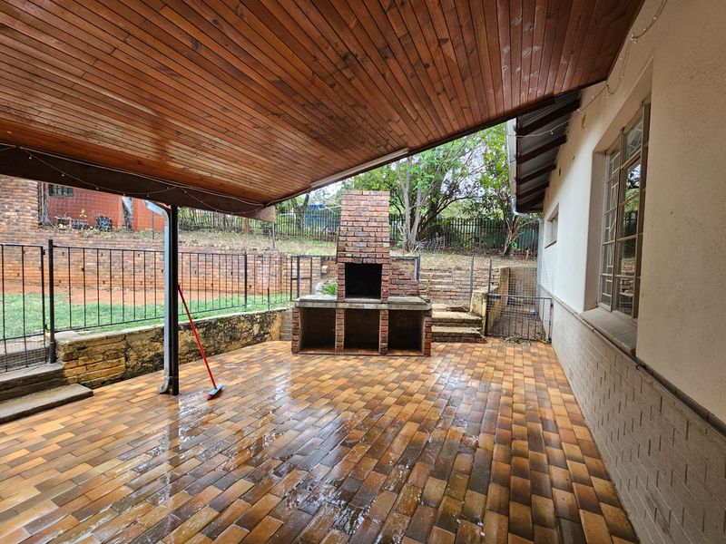 Covered outdoor patio featuring a built-in brick braai, timber ceiling, and paved flooring, overlooking a private garden area.