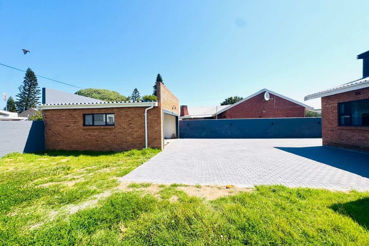 Rear exterior view featuring a brick garage, paved driveway area, and surrounding boundary walls with a grassed yard.