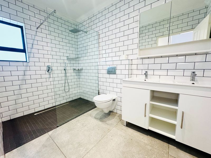 Modern bathroom featuring a spacious walk-in shower with subway tiling, a wall-mounted toilet, and a double vanity with integrated storage.