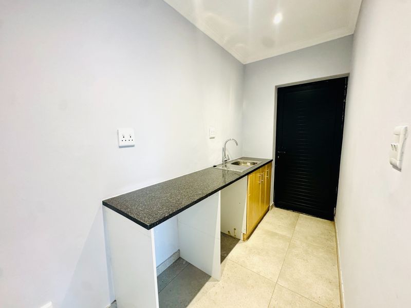 A functional scullery area featuring granite countertops, a stainless steel sink, under-counter cabinetry, and tiled flooring with direct access to the exterior.