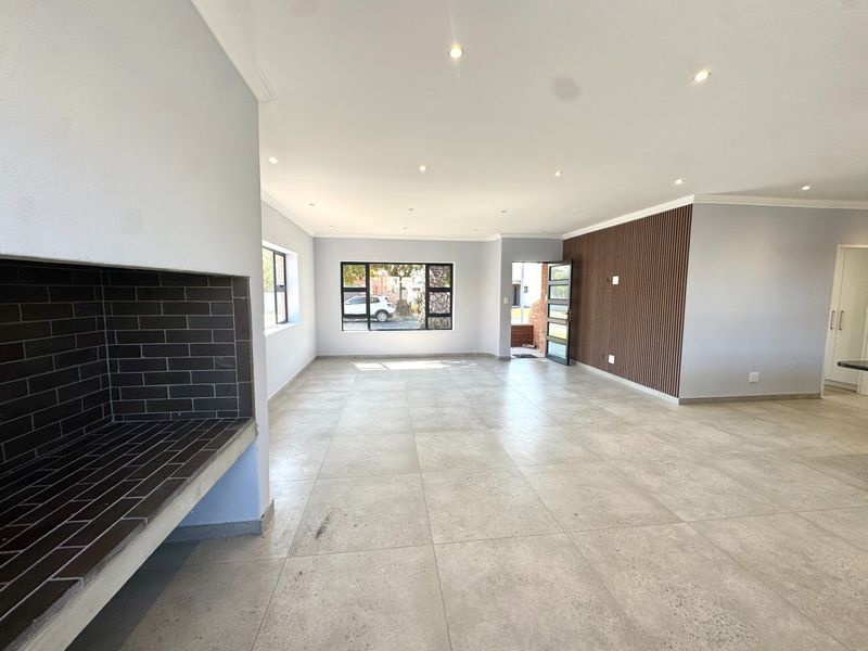 Spacious open-plan living area featuring large format floor tiles, a built-in fireplace, and a modern timber slat feature wall with recessed lighting.