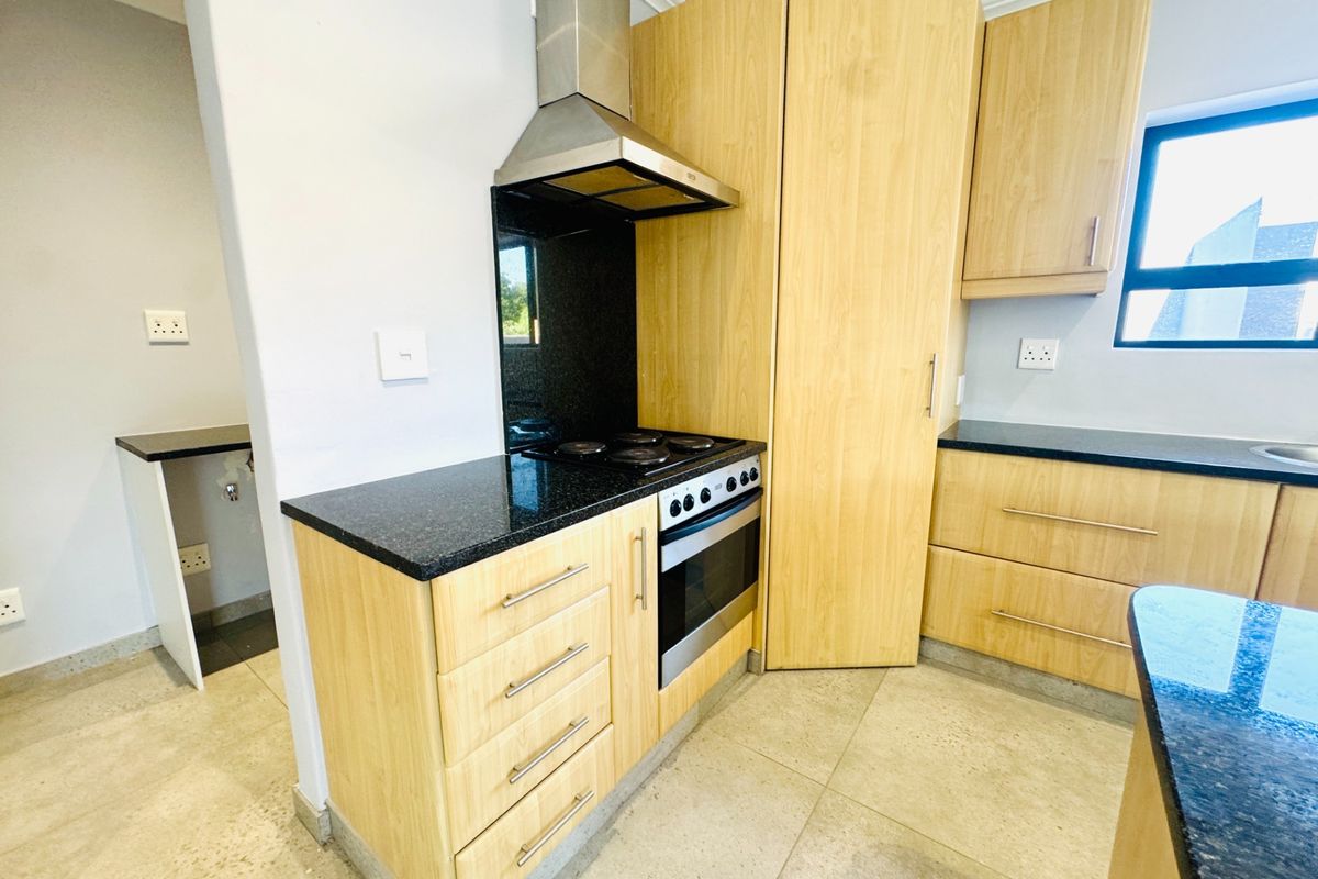 Modern kitchen featuring light wood cabinetry, granite countertops, built-in oven, electric hob, and stainless steel extractor fan with adjacent scullery area.