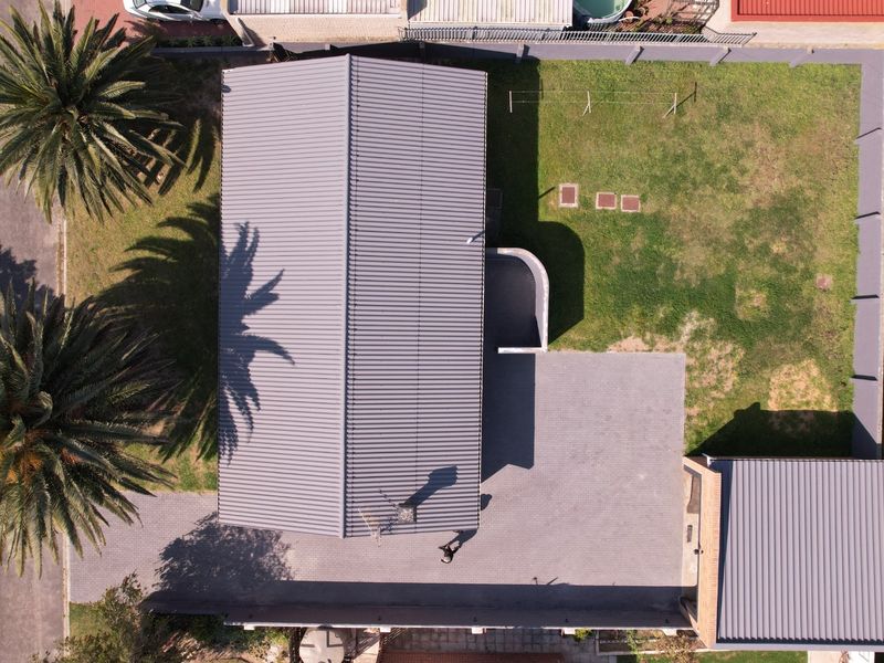 Aerial view of the property showing the main house with a metal roof, paved driveway, detached garage, and surrounding garden area.