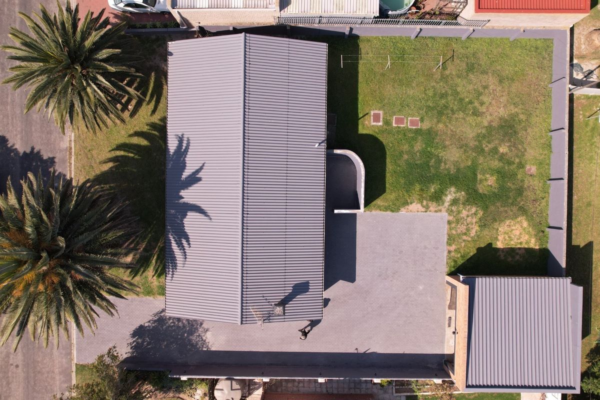 Aerial view of the property showing the main house with a metal roof, paved driveway, detached garage, and surrounding garden area.