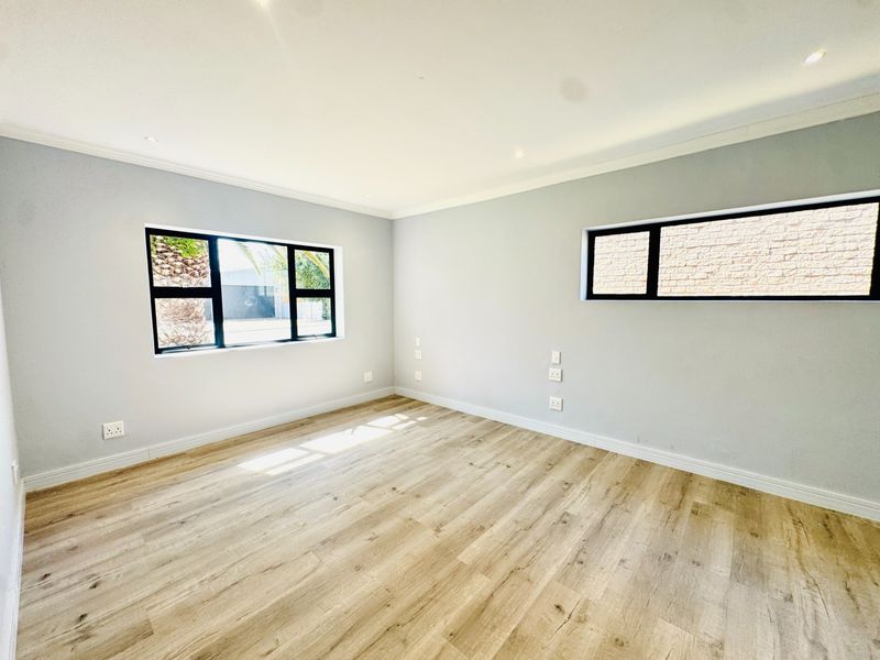 A bright, empty bedroom featuring modern laminate flooring, neutral walls, and black-framed windows, offering a clean and versatile space ready for personalization.