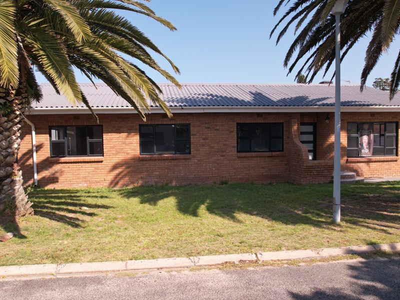 Front elevation of a single-story face brick house featuring a corrugated metal roof and dark aluminium window frames.