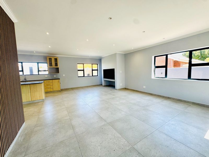 Spacious open-plan living area featuring large format floor tiles, recessed lighting, and a functional kitchen with built-in cabinetry and a dedicated television niche.