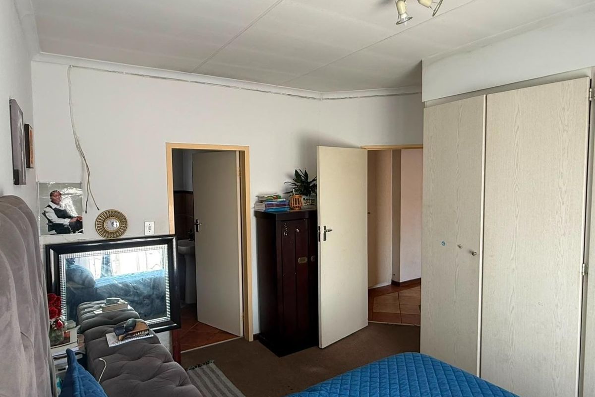 Bedroom featuring built-in cupboards and access to an adjoining bathroom, showing signs of wear and exposed electrical wiring requiring attention.