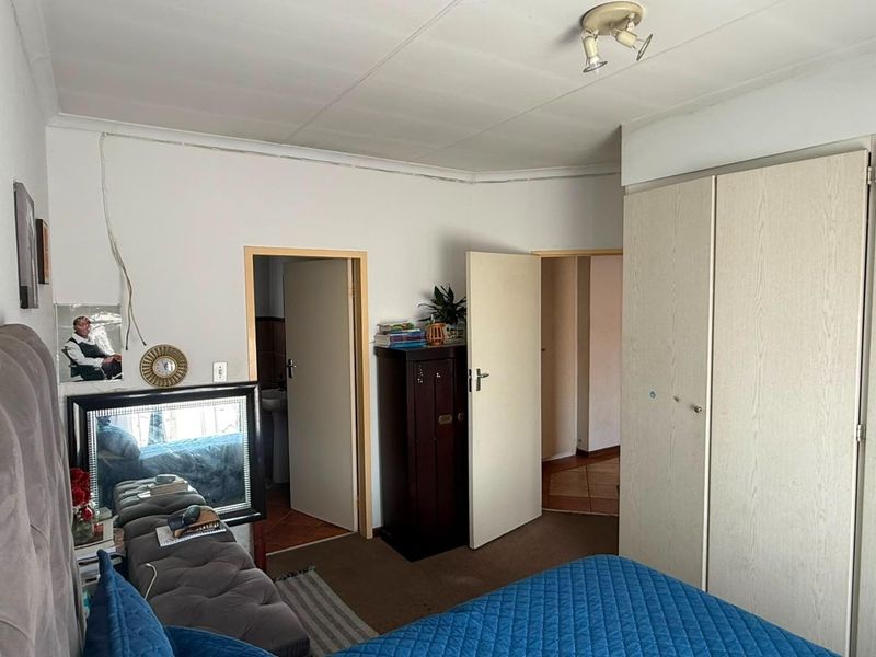 Bedroom featuring built-in cupboards and access to an adjoining bathroom, showing signs of wear and exposed electrical wiring requiring attention.