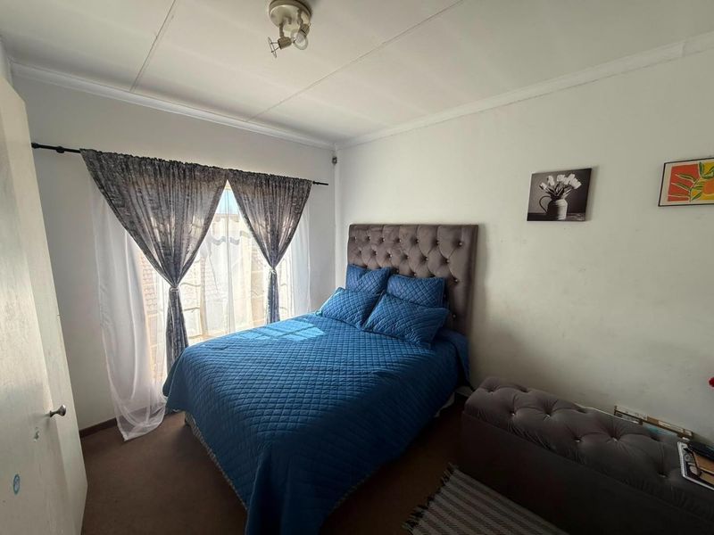 A standard bedroom featuring carpeted flooring, a ceiling light fixture, and a window with installed curtain rods.