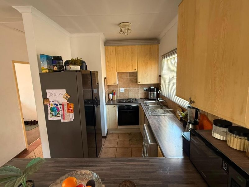 A functional kitchen featuring light wood cabinetry, dark laminate countertops, tiled backsplash, and integrated cooking appliances with tiled flooring.