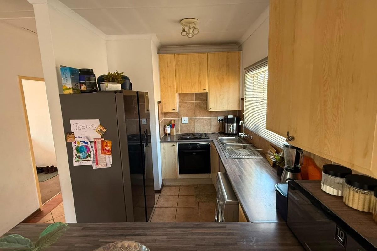 A functional kitchen featuring light wood cabinetry, dark laminate countertops, tiled backsplash, and integrated cooking appliances with tiled flooring.