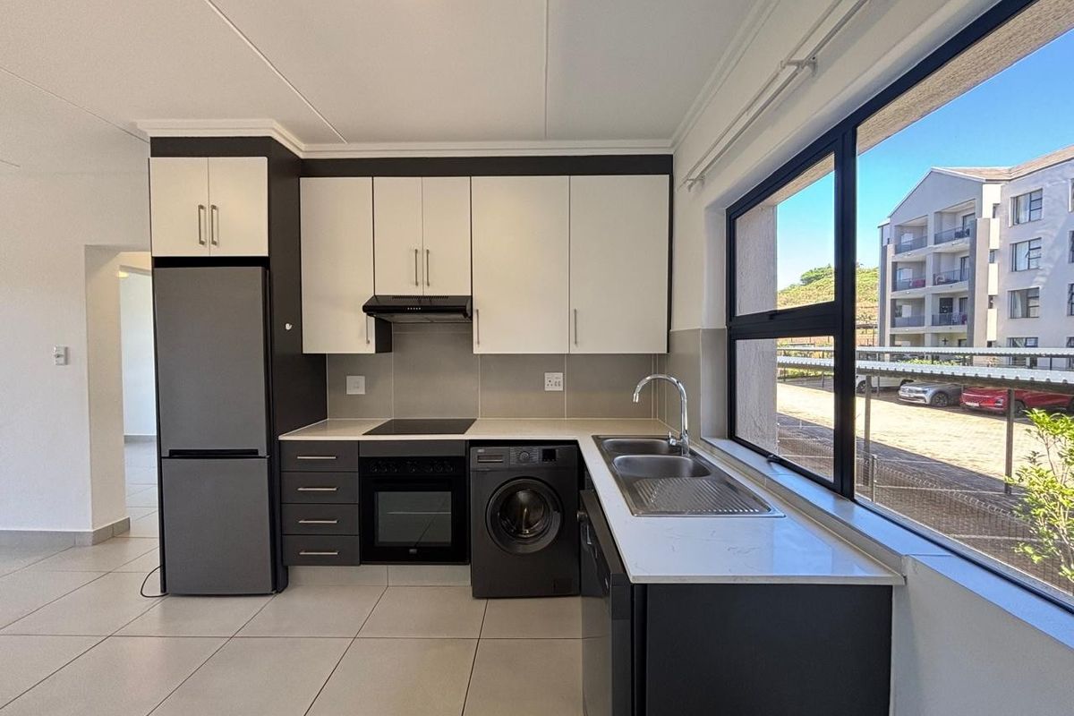 Modern kitchen featuring two-tone cabinetry, stone countertops, integrated oven and hob, and large windows providing ample natural light.