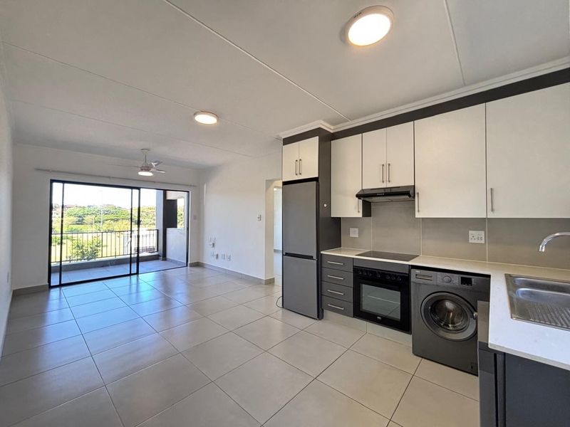 Modern open-plan kitchen and living area featuring tiled floors, built-in cabinetry, integrated appliances, and direct access to a private balcony.
