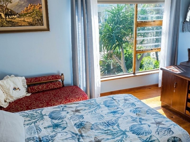 A cozy bedroom featuring warm timber flooring and a large window that provides natural light and a view of the garden.