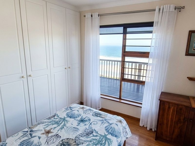 A bright bedroom featuring built-in cupboards, timber flooring, and direct access to a balcony with scenic ocean views.