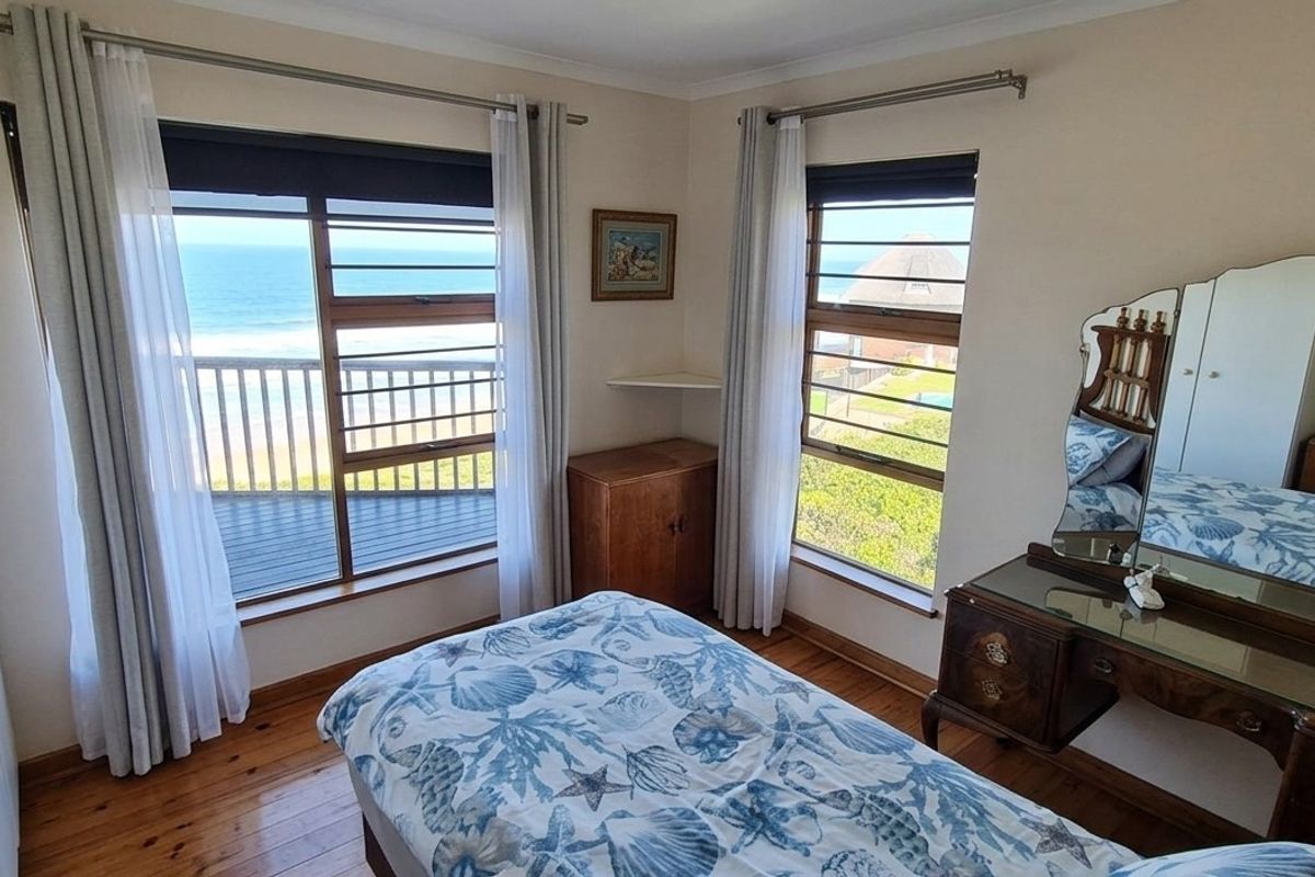 A bedroom featuring timber flooring, built-in cupboards, and large windows offering direct ocean views.