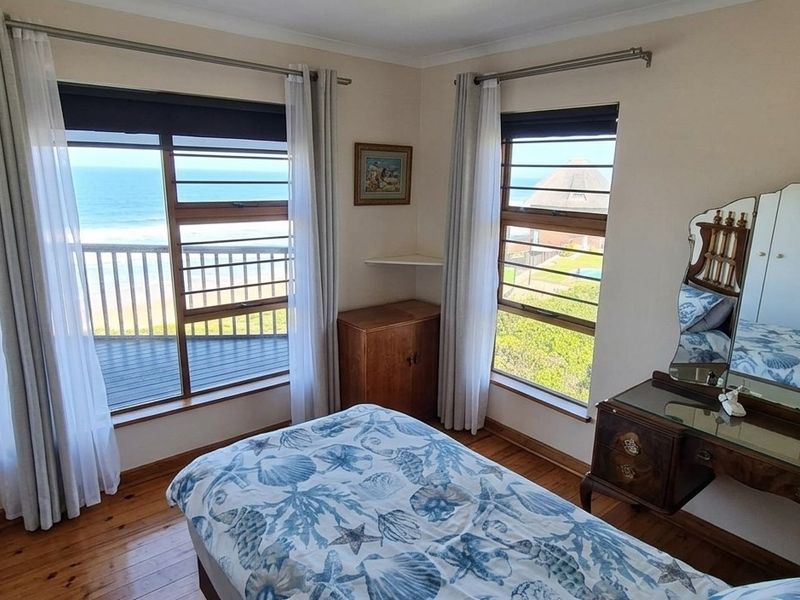 A bedroom featuring timber flooring, built-in cupboards, and large windows offering direct ocean views.