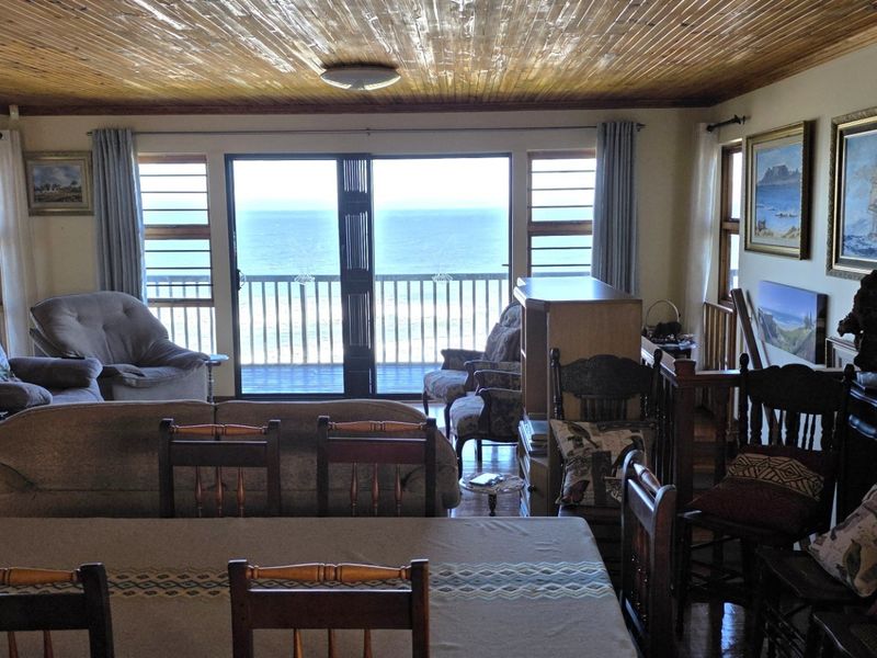 Spacious open-plan living and dining area featuring a timber ceiling and large sliding doors opening to a balcony with ocean views.
