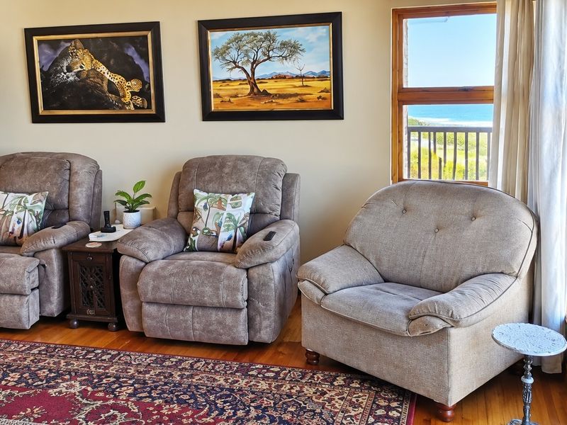 A comfortable living area featuring hardwood flooring and large windows with direct access to an outdoor deck and ocean views.