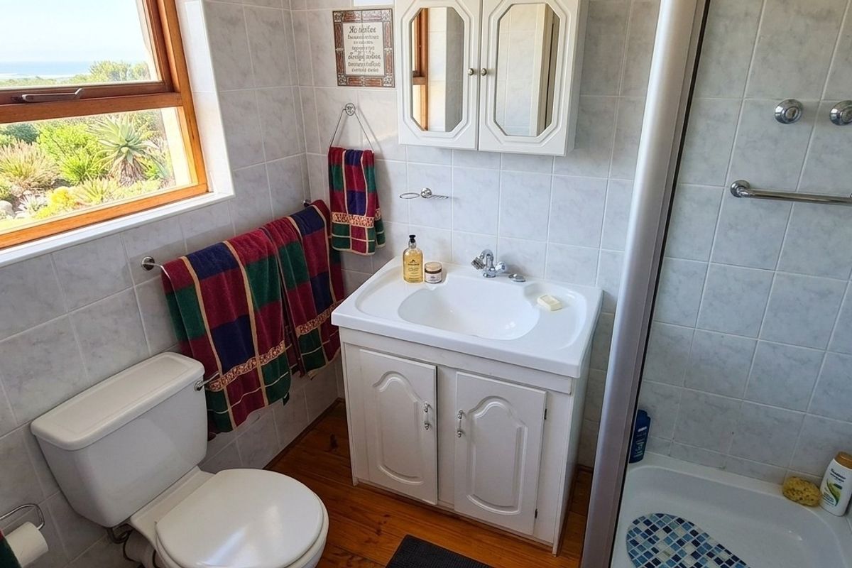 A functional bathroom featuring a vanity cabinet, toilet, and shower enclosure with tiled walls and timber flooring, offering a pleasant garden and coastal view.