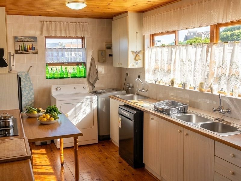 A functional kitchen featuring timber flooring and ceiling, ample cabinetry, double sink, and integrated laundry facilities with natural light.