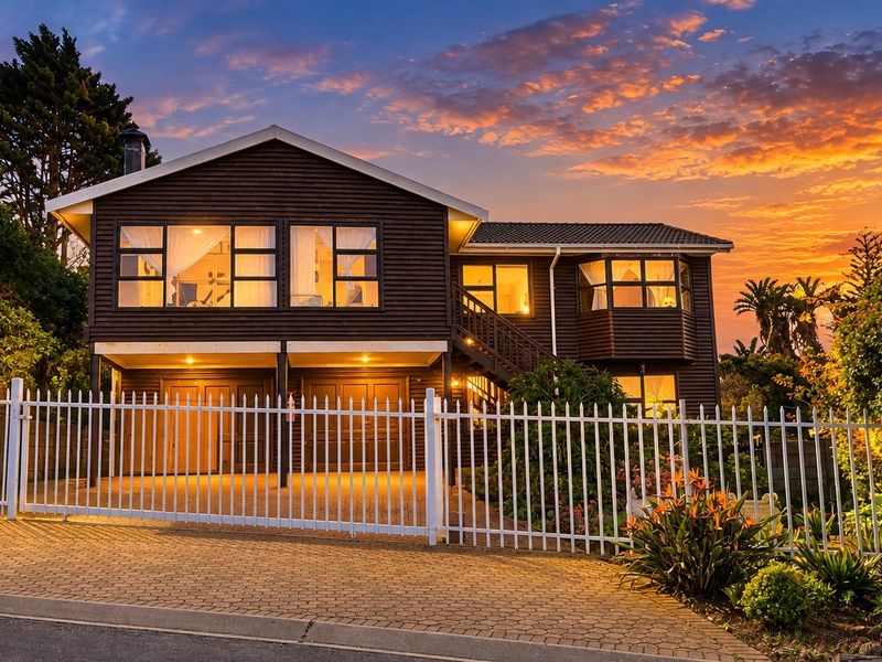 A well-maintained two-story timber-clad house featuring a paved driveway, double garage, and secure metal fencing at sunset.