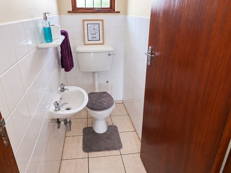 A compact guest bathroom featuring white wall tiles, tiled flooring, a pedestal basin, and a standard toilet.