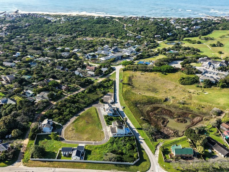 Aerial view of a residential estate featuring vacant land plots, established homes, and proximity to coastal vegetation and golf course facilities.