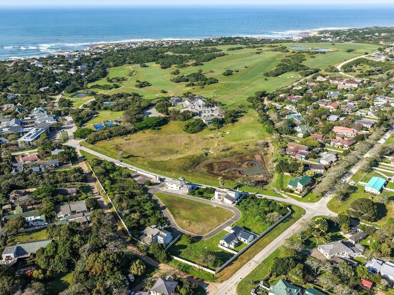Aerial view of a vacant residential plot situated within a coastal estate, featuring established boundary walls and convenient access to local amenities.