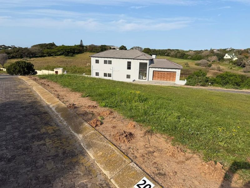A view from the street looking towards a vacant residential plot with a neighboring house in the background.
