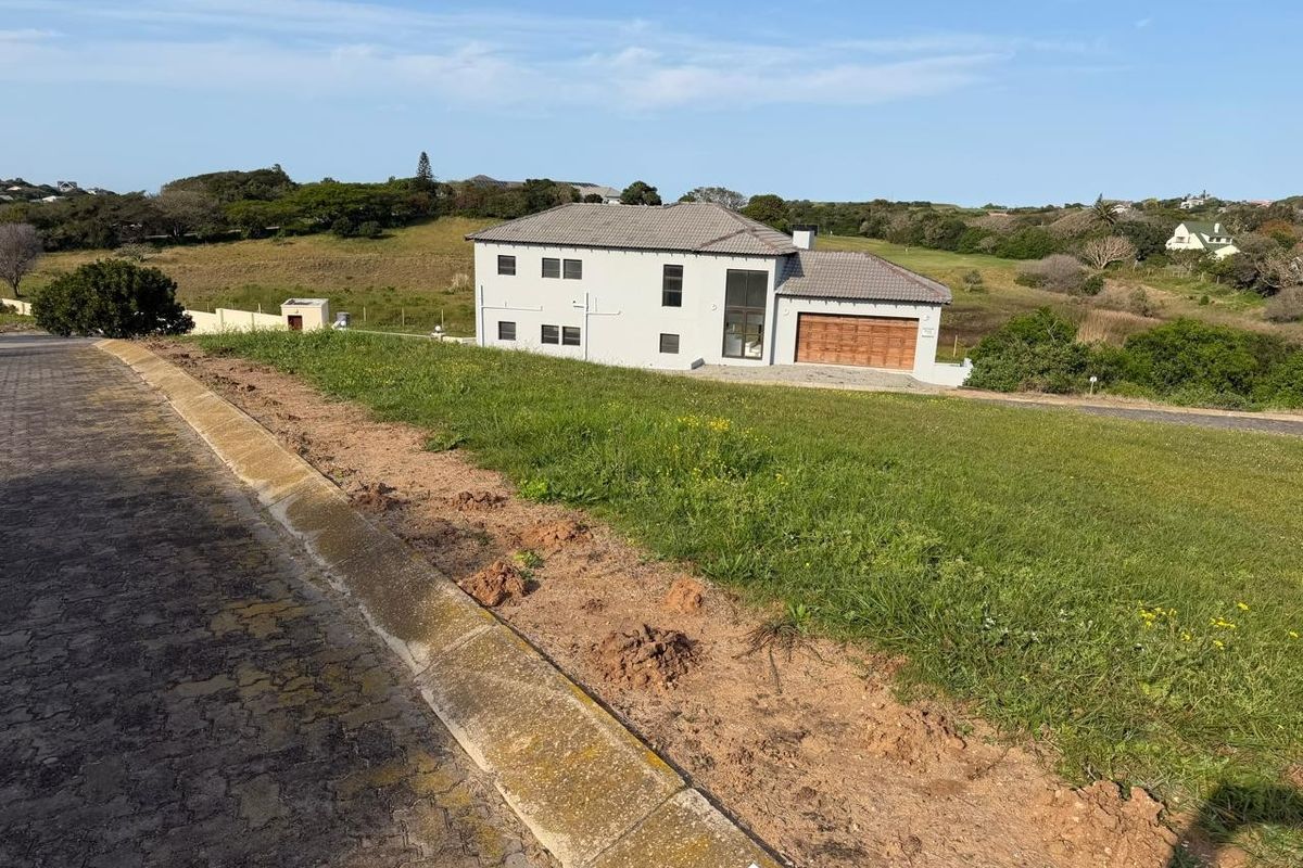 A view from the street looking towards a vacant residential plot with a neighboring house in the background.