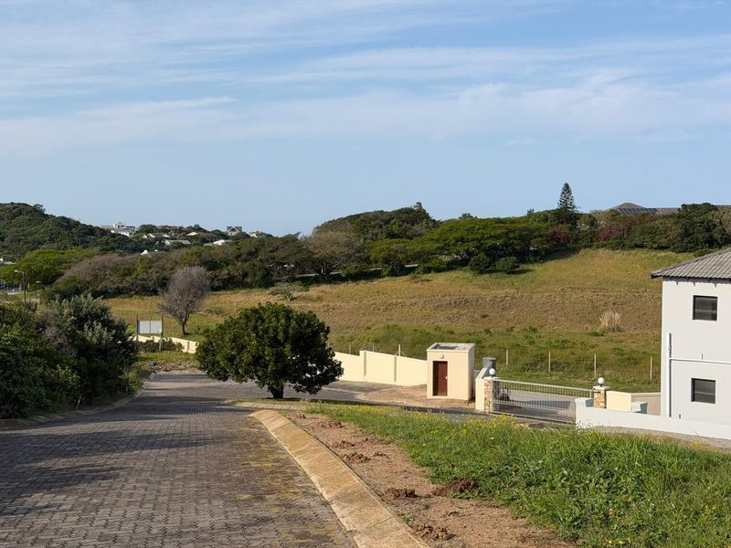 A view of the paved street approach and entrance area of the residential property, featuring boundary walls and a security gate.