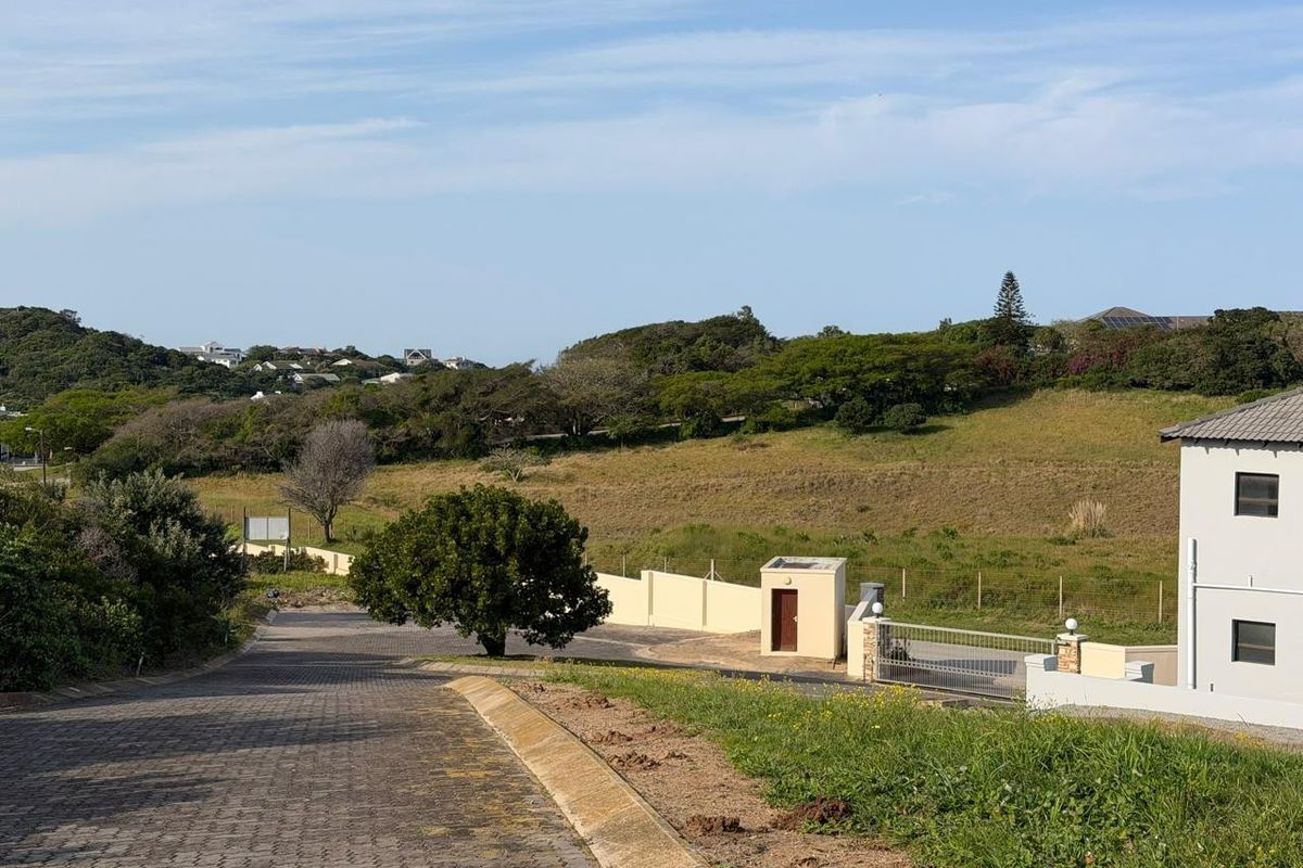 A view of the paved street approach and entrance area of the residential property, featuring boundary walls and a security gate.