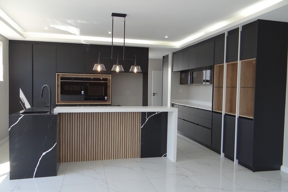 Modern kitchen featuring matte black cabinetry, stone countertops, a central island with slatted wood detailing, and integrated built-in appliances.