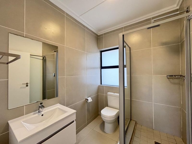 Modern bathroom featuring neutral large-format wall tiles, a sleek vanity with basin, a glass-enclosed shower, and a toilet.