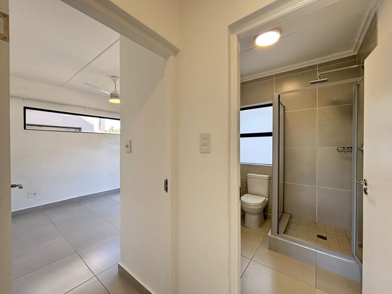 A clean, modern hallway providing access to an adjacent bedroom and a well-maintained bathroom featuring a glass-enclosed shower and neutral tiling.