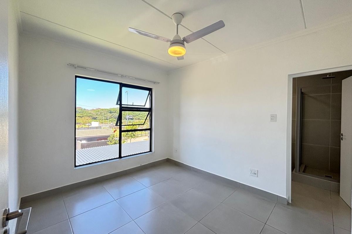 A bright, empty bedroom featuring neutral tiled flooring, a modern ceiling fan, and an en-suite bathroom, offering a clean and versatile living space.