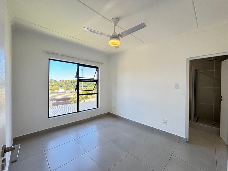 A bright, empty bedroom featuring neutral tiled flooring, a modern ceiling fan, and an en-suite bathroom, offering a clean and versatile living space.