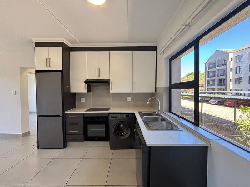 Modern kitchen featuring two-tone cabinetry, stone countertops, integrated oven and hob, and large windows providing ample natural light.