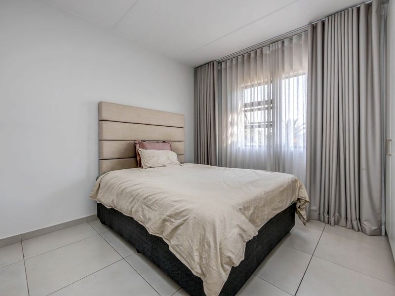 A well-maintained bedroom featuring neutral tiled flooring, a built-in wardrobe, and floor-to-ceiling curtains providing natural light.