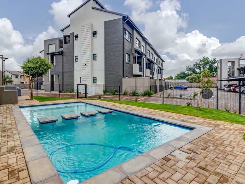 A well-maintained communal swimming pool area featuring paved surrounds, stepped water features, and modern apartment building architecture in the background.