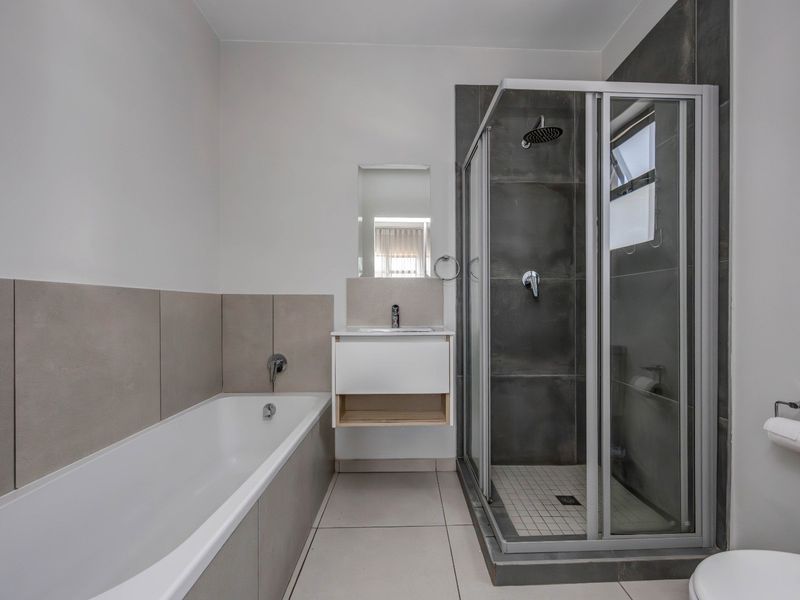 Modern bathroom featuring a separate bathtub, glass-enclosed shower, vanity unit, and neutral-toned wall and floor tiling.