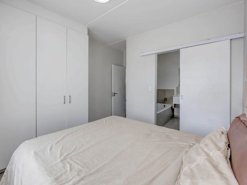 A bright bedroom featuring built-in cupboards and a sliding door providing direct access to an en-suite bathroom.