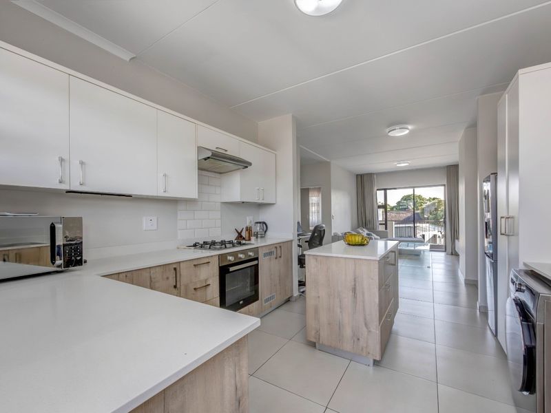 Modern open-plan kitchen featuring light wood cabinetry, stone countertops, gas hob, and integrated appliances, flowing into a bright living area with balcony access.