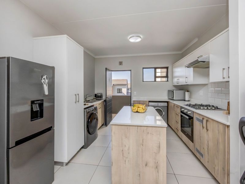 Modern kitchen featuring light wood-finish cabinetry, stone countertops, a central island, built-in gas hob, oven, and integrated laundry plumbing.