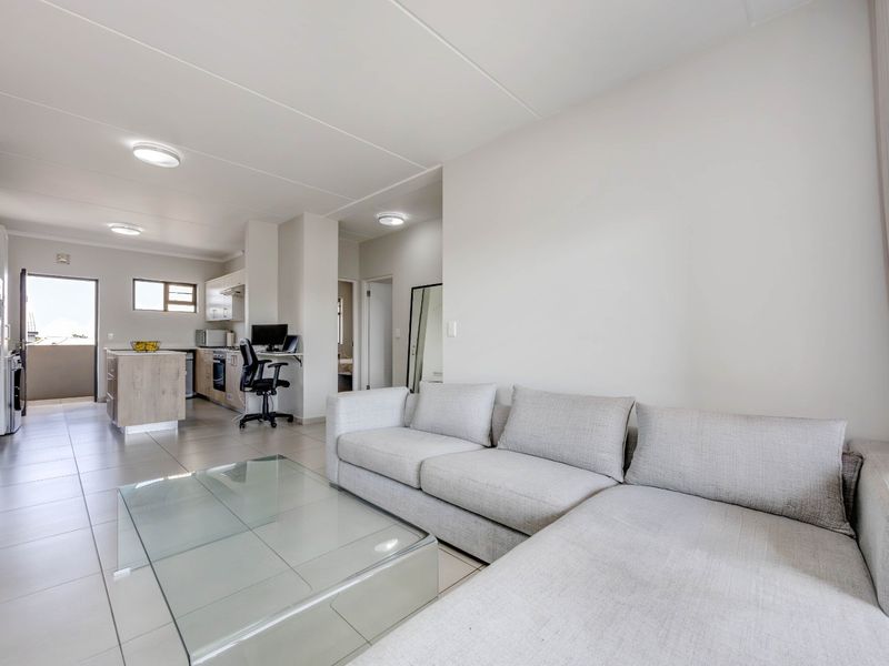Modern open-plan living area featuring tiled floors, a functional kitchen with built-in cabinetry, and seamless access to an outdoor balcony.